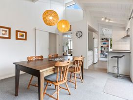 A dining area with wooden table and chairs two pendant lights and a view into a kitchen and living room at Waiake Family Retreat Auckland