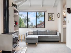 A living room with a gray sectional sofa a wood stove bookshelf and a large window at Waiake Family Retreat Auckland