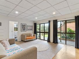A living room with two sofas a round rug sliding glass doors with dark curtains and framed pictures on the wall at Waiake Family Retreat Auckland Holiday Home in Auckland