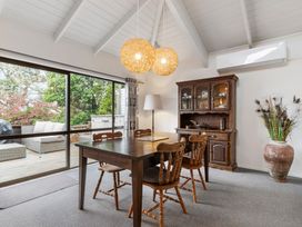 A dining room with wooden table four chairs a cabinet floor lamp vase and large sliding glass doors at Waiake Family Retreat Auckland Holiday Home in Auckland