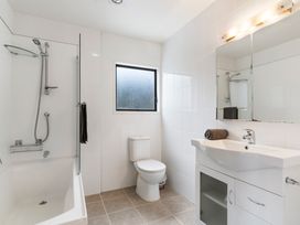 A bathroom with a bathtub and shower head a toilet a sink with a cabinet and a mirror above it at Waiake Family Retreat Auckland