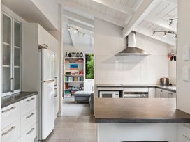 A kitchen with white cabinets a refrigerator a microwave and an oven with a vent hood and a view into a living room with a bookshelf and a gray sofa at Waiake Family Retreat - Auckland Holiday Home in Auckland