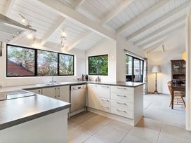 A kitchen with white cabinets gray countertops and large windows overlooking trees at Waiake Family Retreat Auckland Holiday Home
