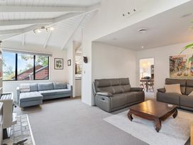 A living room with two leather sofas a wooden coffee table and a fabric sofa near a large window at Waiake Family Retreat in Auckland