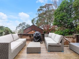 An outdoor deck with two sofas a coffee table a covered grill and trees at Waiake Family Retreat Auckland Holiday Home in Auckland