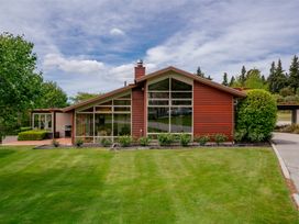 A red wooden house with large windows and a green lawn in front at Elderberry Wine Wanaka Holiday Home