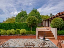 An outdoor patio area with a tiled table and metal chairs next to trimmed bushes and a staircase leading to a building at Elderberry Wine - Wanaka Holiday Home in Wanaka