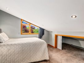 A bedroom with a bed under a sloped ceiling near a window and a low cupboard at Elderberry Wine - Wanaka Holiday Home in Wanaka