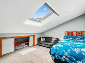 A bedroom with a skylight window a black couch two pillows a colorful bed headboard and blue floral bedding at Elderberry Wine - Wanaka Holiday Home in Wanaka