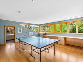 A game room with a ping pong table a desk with office supplies and large windows overlooking greenery at Elderberry Wine - Wanaka Holiday Home in Wanaka