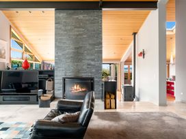 A living room with a stone fireplace a leather armchair and a television at Elderberry Wine - Wanaka Holiday Home Wanaka