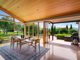 A dining area with table and chairs near large glass windows and open doors leading to a patio with barbecue at Elderberry Wine - Wanaka Holiday Home in Wanaka