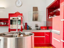 A kitchen with red cabinets a round stainless steel sink a wall clock and a stovetop with a hood at Elderberry Wine - Wanaka Holiday Home in Wanaka