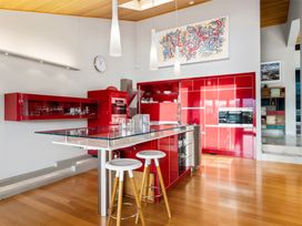 A kitchen with red cabinets a glass countertop island with two stools and wall art at Elderberry Wine - Wanaka Holiday Home Wanaka