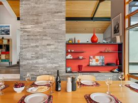 A dining table set with plates wine glasses grape bowl and bottles in front of a stone wall and red shelves at Elderberry Wine - Wanaka Holiday Home Wanaka
