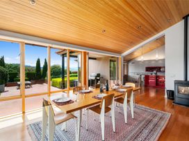 A dining area with a wooden table and chairs set with plates and glasses next to large glass doors opening to a patio with a grill and garden at Elderberry Wine - Wanaka Holiday Home in Wanaka