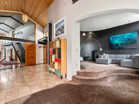 A living room with a stepped carpeted floor gray sectional sofa and a large wall art at Elderberry Wine - Wanaka Holiday Home in Wanaka