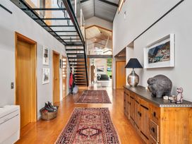 A hallway with wooden floors and doors rugs a wooden cabinet with decorations and a glass staircase Elderberry Wine Wanaka Holiday Home Wanaka