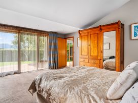 A bedroom with a bed a wooden wardrobe curtains and a door leading outside at Elderberry Wine - Wanaka Holiday Home in Wanaka