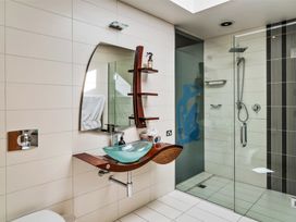 A bathroom with a glass sink on a wooden countertop a wall-mounted mirror a towel a walk-in shower with glass doors and a rainfall showerhead at Elderberry Wine - Wanaka Holiday Home in Wanaka