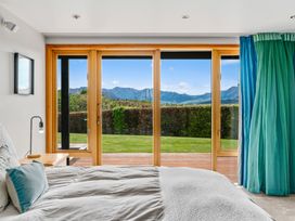 A bedroom with a bed bedside table lamp large sliding glass doors opening to a garden with mountains in the distance at Elderberry Wine - Wanaka Holiday Home Wanaka