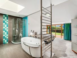 A bedroom with a bed and nightstands connected to a bathroom with a bathtub and a glass shower at Elderberry Wine - Wanaka Holiday Home in Wanaka