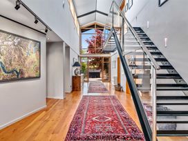 A hallway with wooden floors red rugs a side table with a lamp a map on the wall and a staircase with glass railing at Elderberry Wine - Wanaka Holiday Home in Wanaka