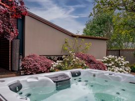 An outdoor hot tub surrounded by bushes and plants next to a beige wall with trees in the background at Elderberry Wine - Wanaka Holiday Home Wanaka