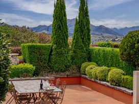 An outdoor patio area with a table and chairs surrounded by neatly trimmed hedges and trees with mountains in the background at Elderberry Wine - Wanaka Holiday Home in Wanaka