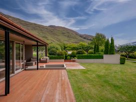 A wooden deck with outdoor seating adjacent to a grassy lawn and landscaped bushes at Elderberry Wine - Wanaka Holiday Home Wanaka