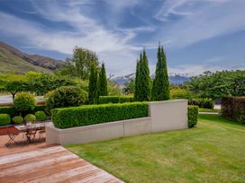 A garden with manicured hedges trees and outdoor seating with mountains in the background at Elderberry Wine Wanaka Holiday Home Wanaka
