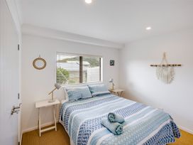 A bedroom with a bed and blue patterned bedding two towels on the bed two bedside tables with lamps a window with blinds and wall decorations at Sunset Haven - Mahia Holiday Home in Mahia Peninsula
