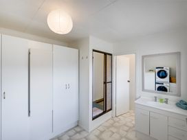 A laundry room with white cabinets a sink with a mirror above and a washing machine and dryer reflected in the mirror at Sunset Haven - Mahia Holiday Home in Mahia Peninsula
