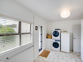 A laundry room with stacked washer and dryer a tall white cabinet a window with blinds and a door at Sunset Haven - Mahia Holiday Home in Mahia Peninsula
