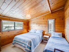 A bedroom with wooden walls and ceiling with a double bed and a single bed with blue and white bedspreads and a white nightstand with a lamp at Sunset Haven Mahia Holiday Home Mahia Peninsula