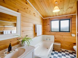 A bathroom with wooden walls a bathtub a sink with a plant a towel rack and a window at Sunset Haven Mahia Peninsula
