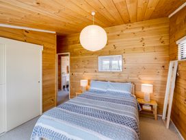 A bedroom with a bed a bedside table with lamps a standing mirror and wooden walls at Sunset Haven Mahia Holiday Home Mahia Peninsula