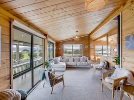 A wooden living room with sofa armchairs and large windows at Sunset Haven Mahia Holiday Home Mahia Peninsula