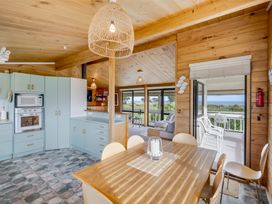 A kitchen and dining area with wooden walls and ceiling adjacent to a living room and outdoor patio at Sunset Haven Mahia Holiday Home Mahia Peninsula