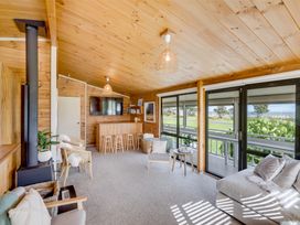 A living room with wooden walls ceiling a wood stove a TV a bar with stools and large sliding glass doors at Sunset Haven - Mahia Holiday Home in Mahia Peninsula