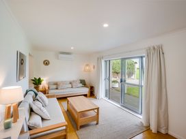 A living room with two sofas a wooden coffee table a lamp and sliding glass doors with curtains at Sunset Haven - Mahia Holiday Home in Mahia Peninsula