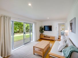 A living room with a sofa a wooden coffee table a tv mounted on the wall and sliding glass doors at Sunset Haven - Mahia Holiday Home in Mahia Peninsula