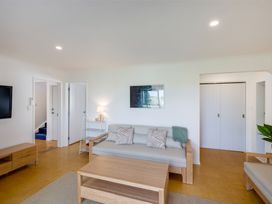 A living room with a wooden coffee table a light grey sofa with cushions a small white shelving unit a wooden TV stand and white walls at Sunset Haven - Mahia Holiday Home Mahia Peninsula