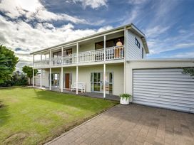 A two-story house with a balcony a lawn a driveway and a closed garage door at Sunset Haven - Mahia Holiday Home in Mahia Peninsula