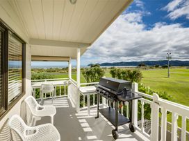 A balcony with white chairs a barbecue grill and a view of grass and mountains at Sunset Haven - Mahia Holiday Home in Mahia Peninsula