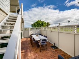 An outdoor patio area with a rectangular table and eight chairs surrounded by a white fence and a staircase on the left at Sunset Haven Mahia Holiday Home Mahia Peninsula