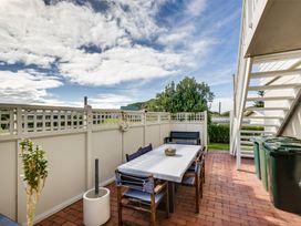 An outdoor patio area with a long table covered with a white cloth surrounded by chairs and a bench under a staircase with green garbage bins Sunset Haven - Mahia Holiday Home Mahia Peninsula
