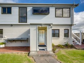 Exterior view of a two-story house with a small porch entrance and outdoor sink with a brick patio at Sunset Haven - Mahia Holiday Home in Mahia Peninsula