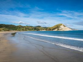 A sandy beach with gentle waves and hills in the background at Sunset Haven Mahia Holiday Home in Mahia Peninsula