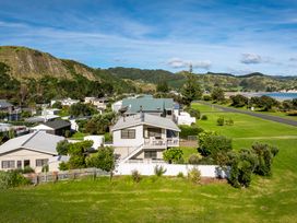 A coastal residential area with houses surrounded by green hills and a road near the ocean at Sunset Haven - Mahia Holiday Home in Mahia Peninsula